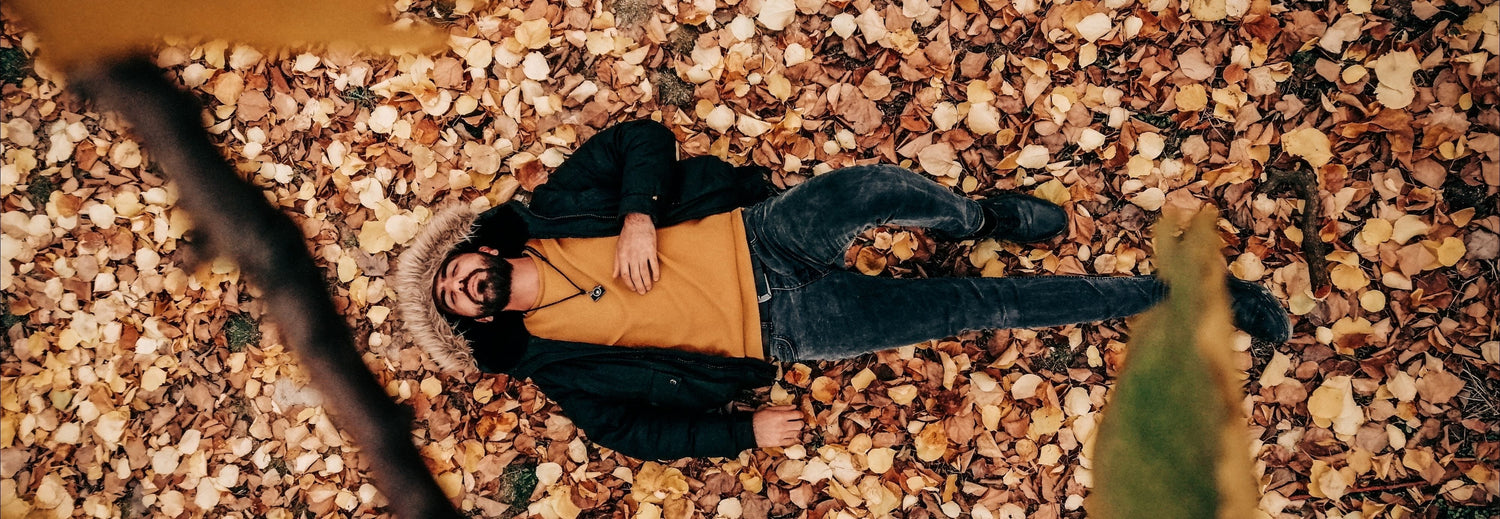 Man outside lying on fall leaves and looking exhausted