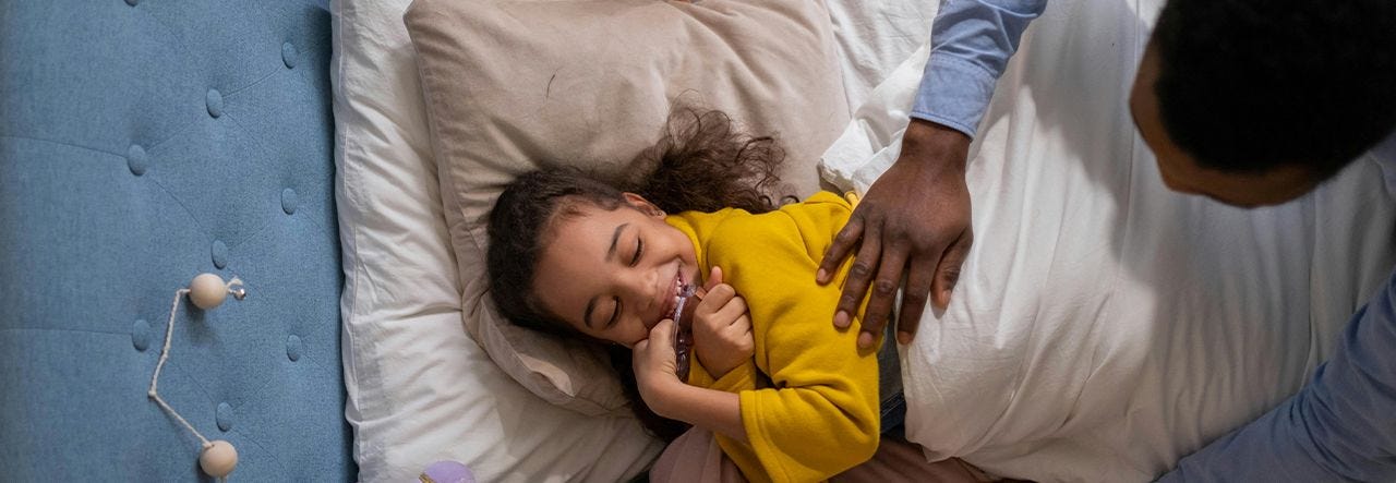 2 to 4 year old child smiling in bed while being tucked in