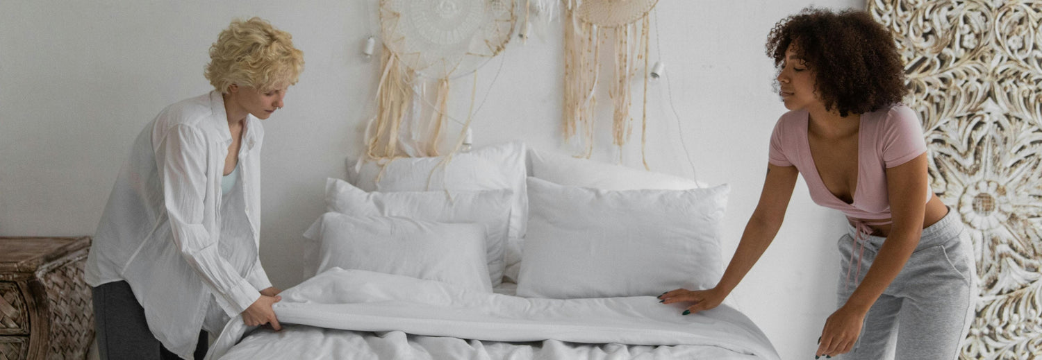two women putting sheets on a bed