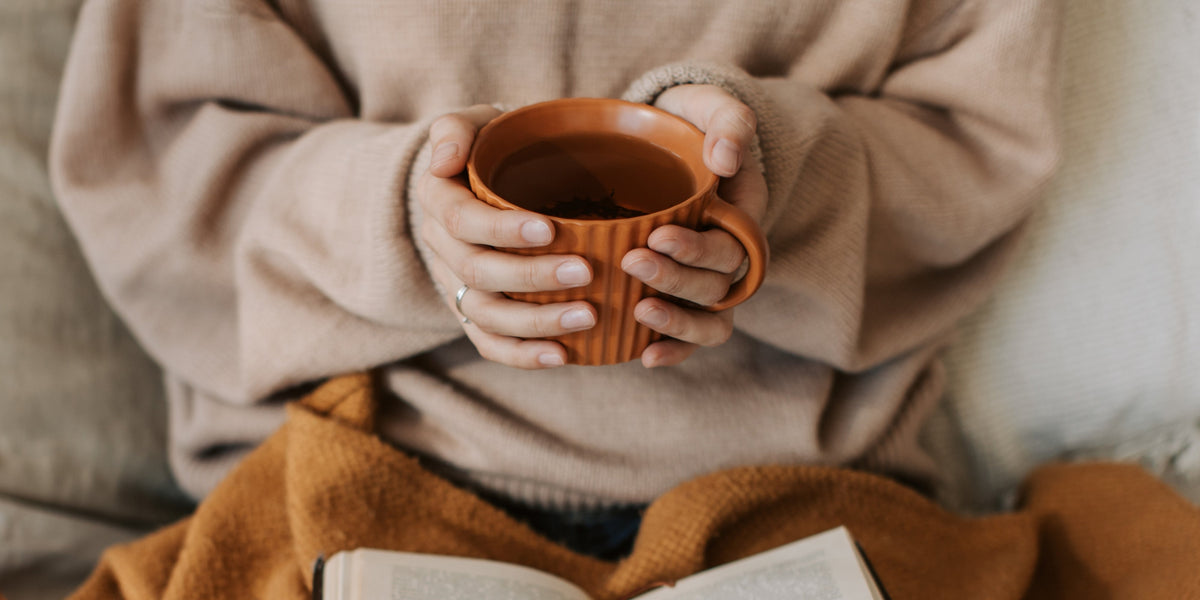 Hands holding cup of coffee in bed