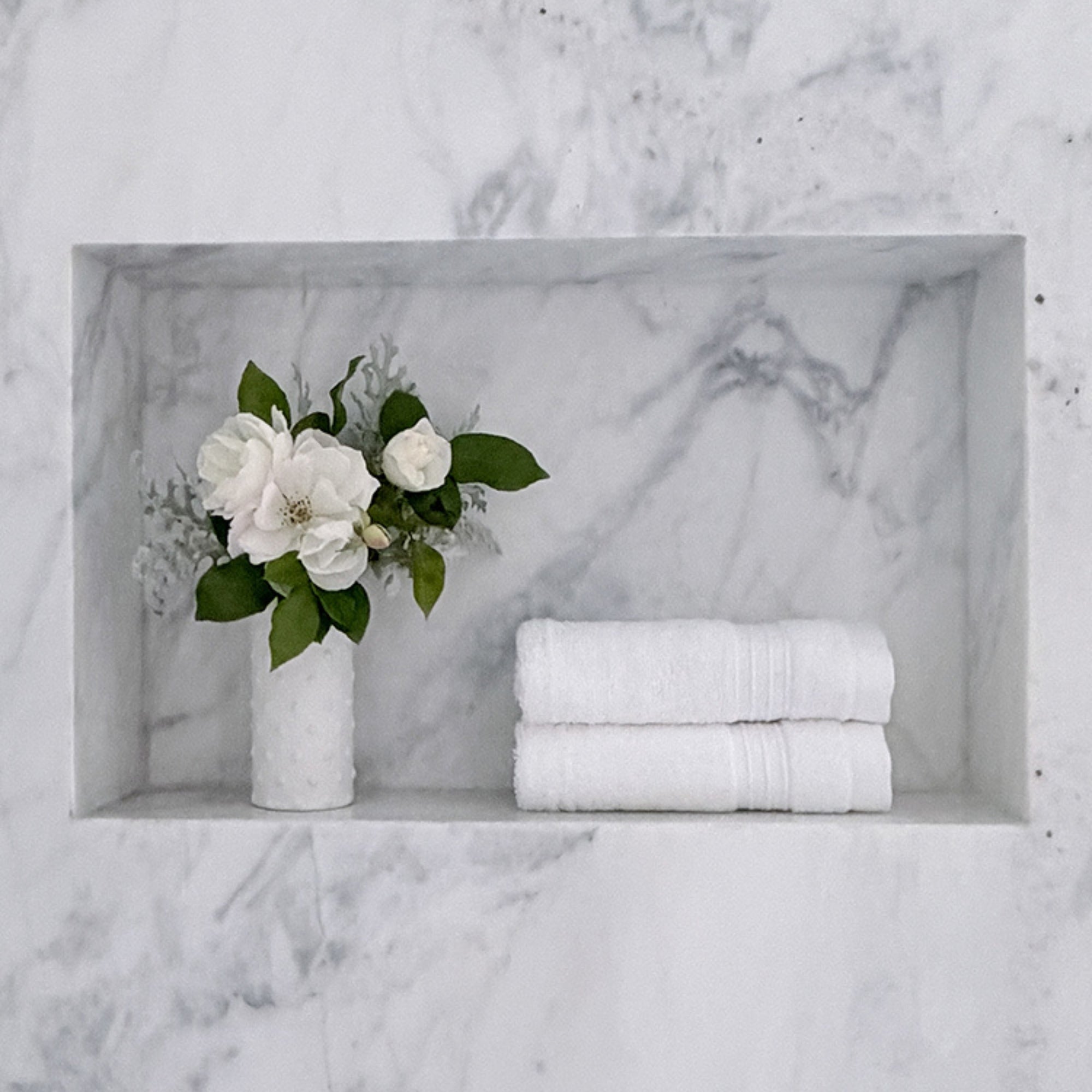 White towels and a vase with white flowers on a marble shelf