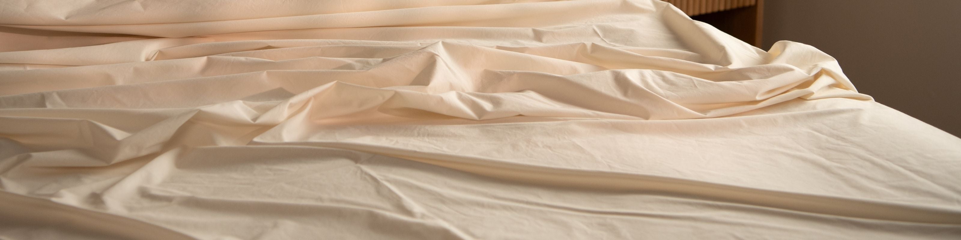 Sateen bed sheets in natural on a bed with a wooden headboard.