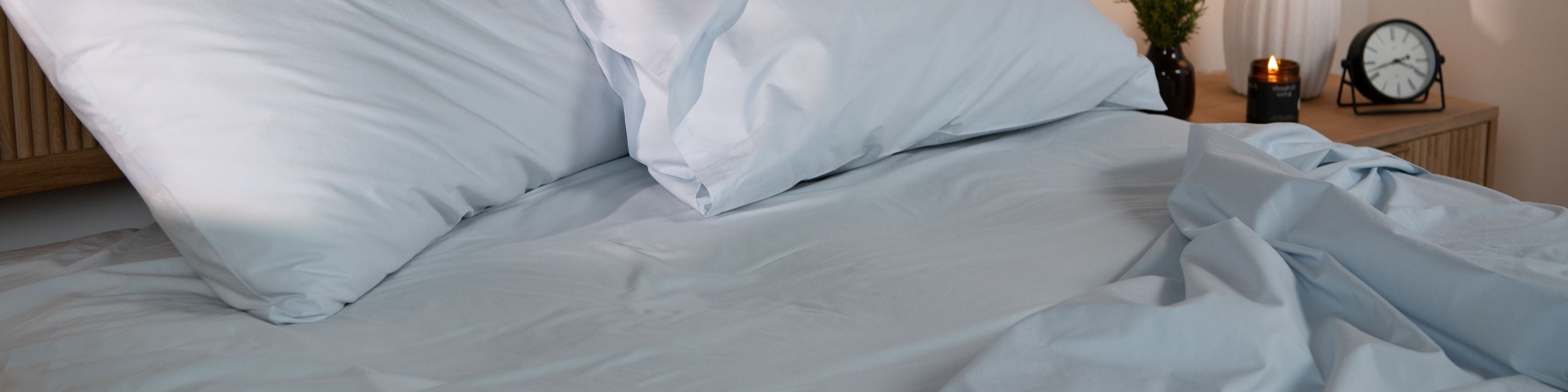 Neatly made bed with pillows and light blue sheets in a bedroom setting.