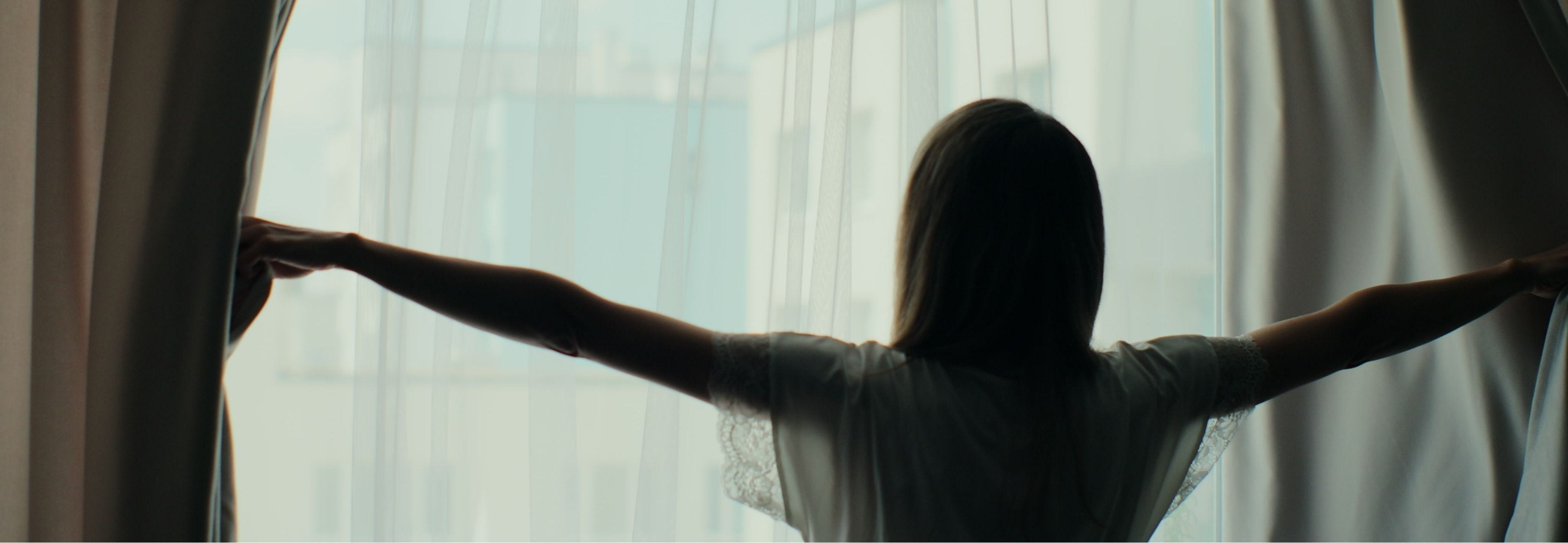 woman opening the blinds in the morning