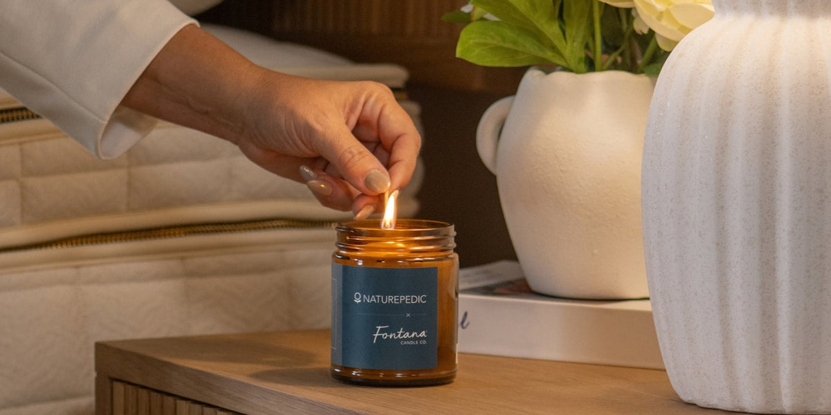 person lighting a naturepedic x fontana candle bedside