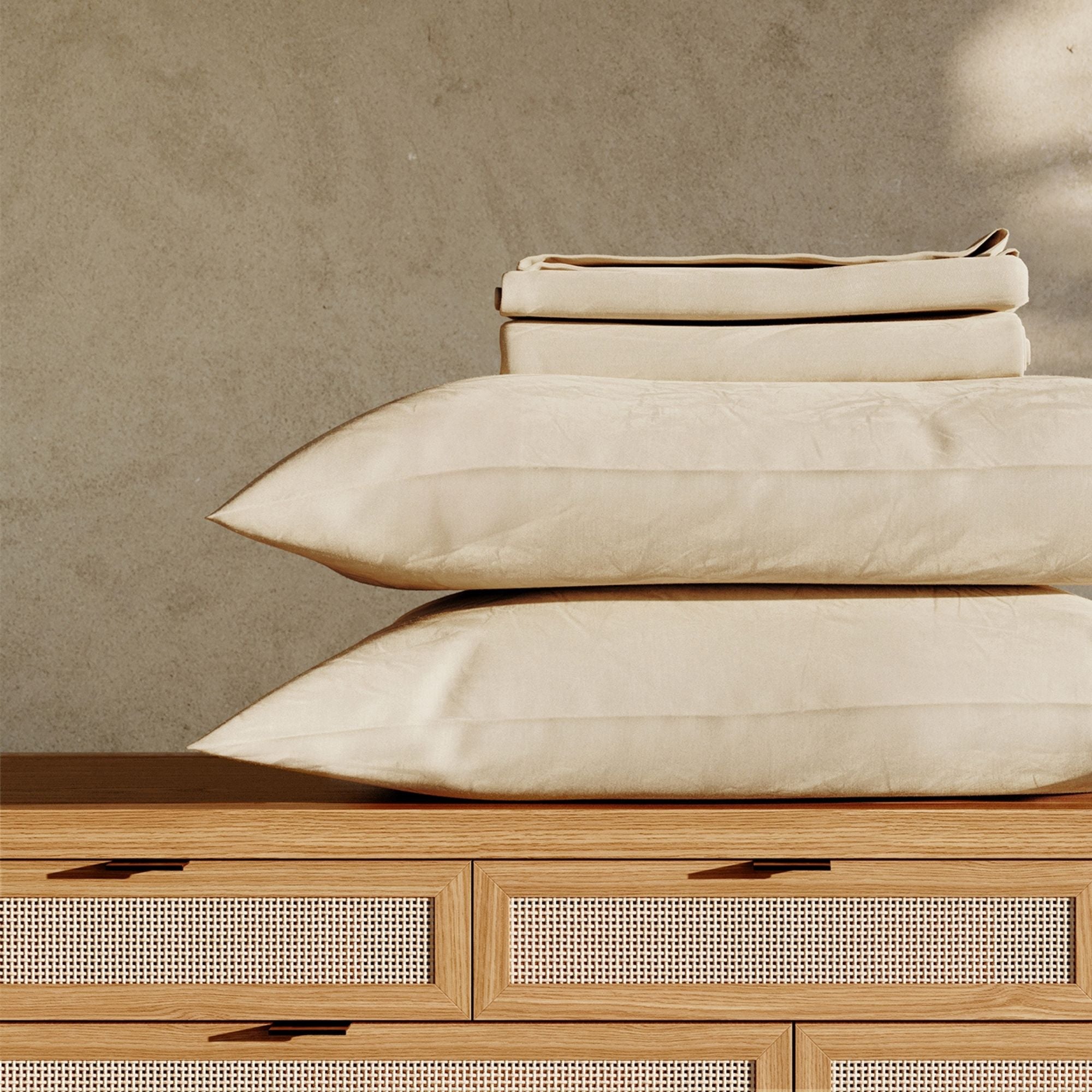 Beige pillows and sheets, stacked on a wooden bed with a neutral background #color_undyed