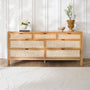 Wooden dresser with woven drawers in a room with light-colored walls and flooring.