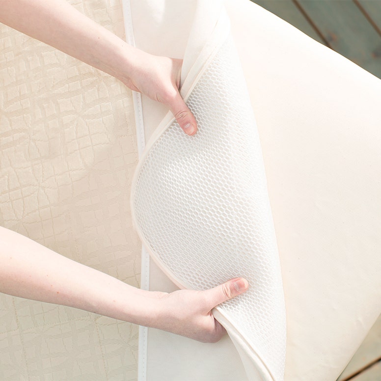 Breathable cover pulled back over crib mattress corner showing underside