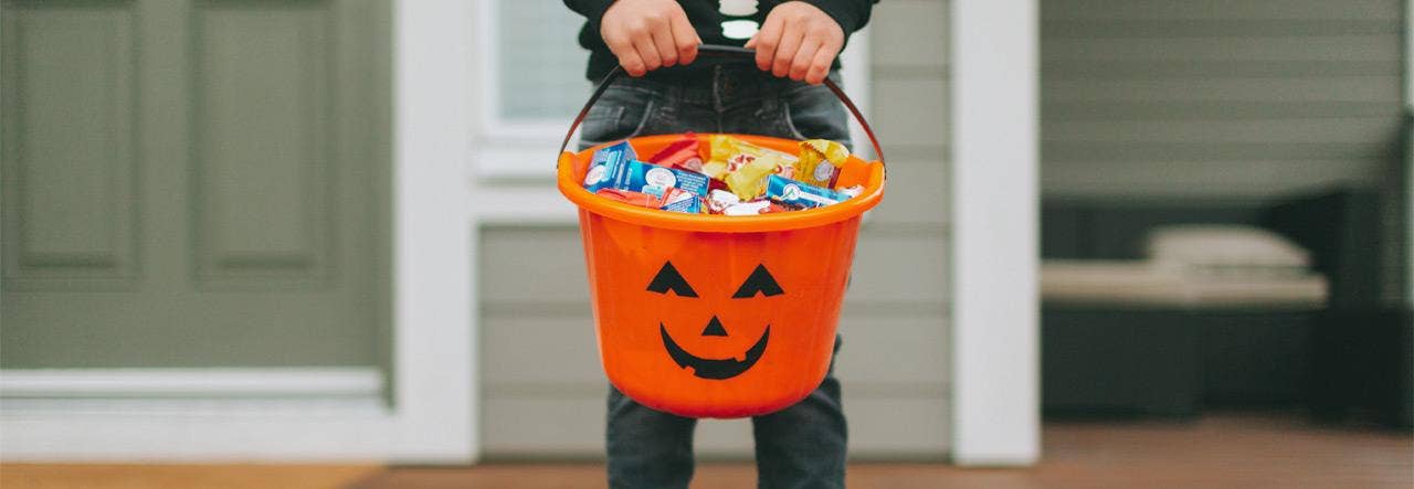 Child from the neck down in skeleton costume holding and orange bucket of candy 