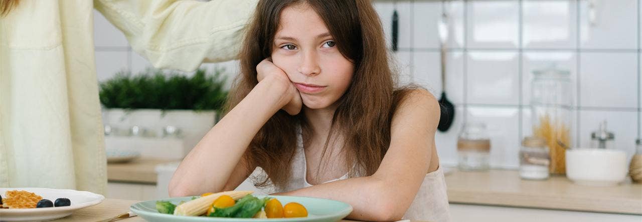 Girl with chin in hand, unhappy face, with plate of vegetables