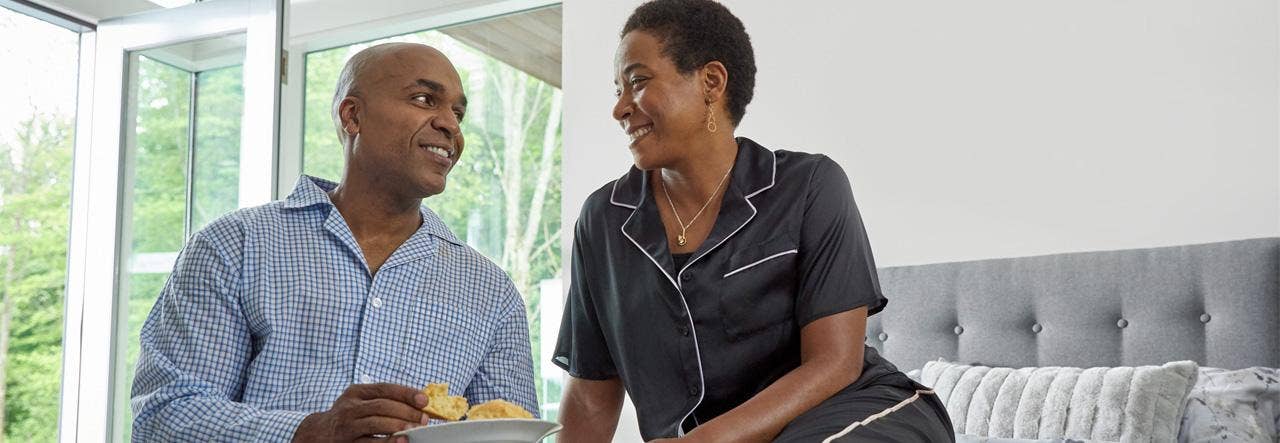 Couple eating breakfast in bed and smiling at one another