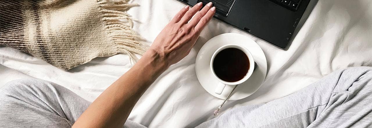 Overhead image of a woman on a laptop and sitting cross-legged with a cup of coffee