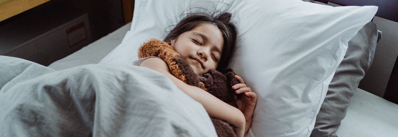 School-aged girl sleeping in bed, hugging a soft toy