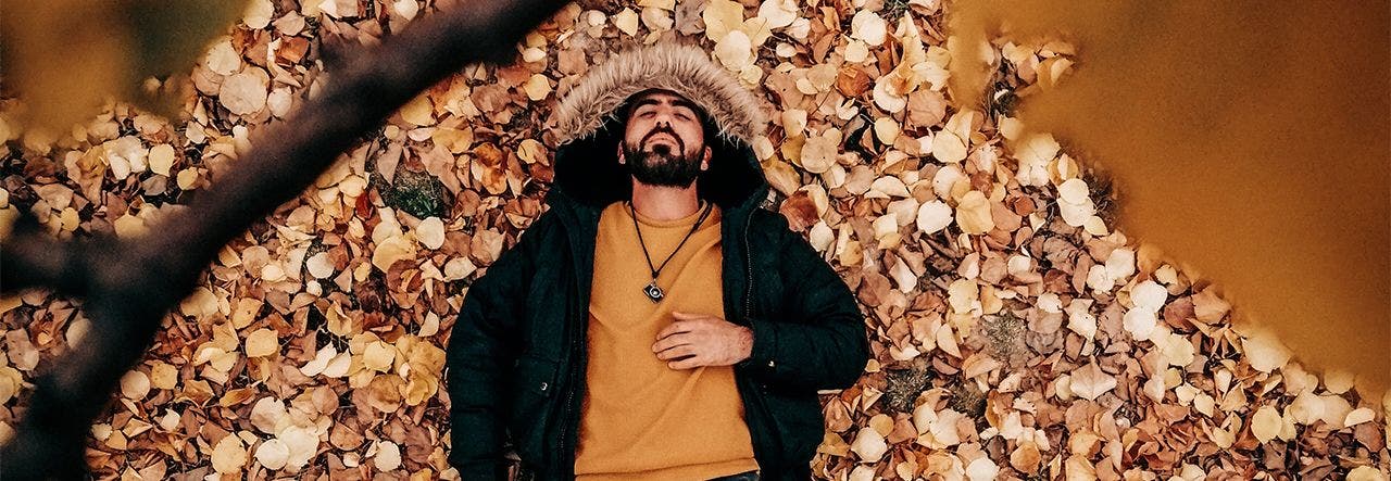 Man outside lying on fall leaves and looking exhausted