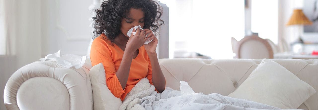 Woman sitting on the couch under a blanket, blowing her nose