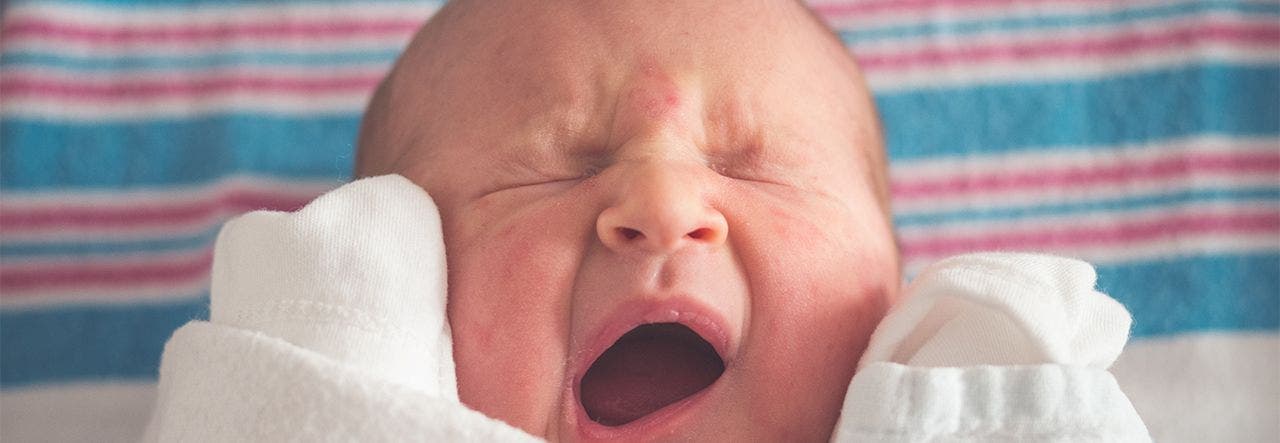 Newborn baby yawning with eyes tightly shut