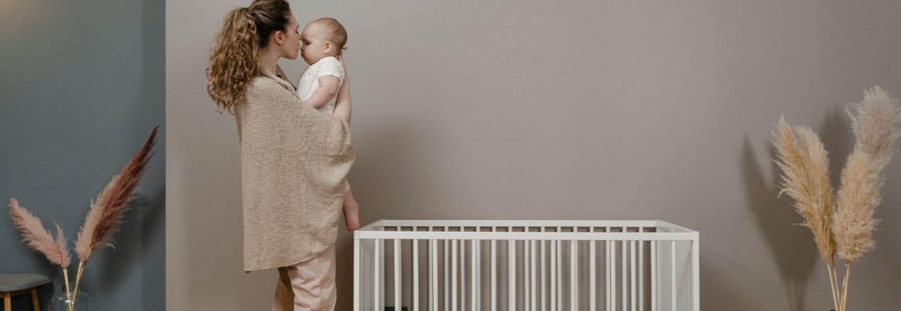 Mother standing near crib and cuddling her baby