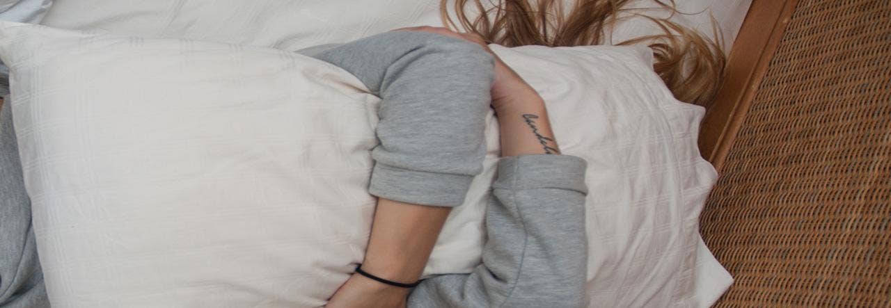 Frustrated, tired woman holding her pillow over her face in bed