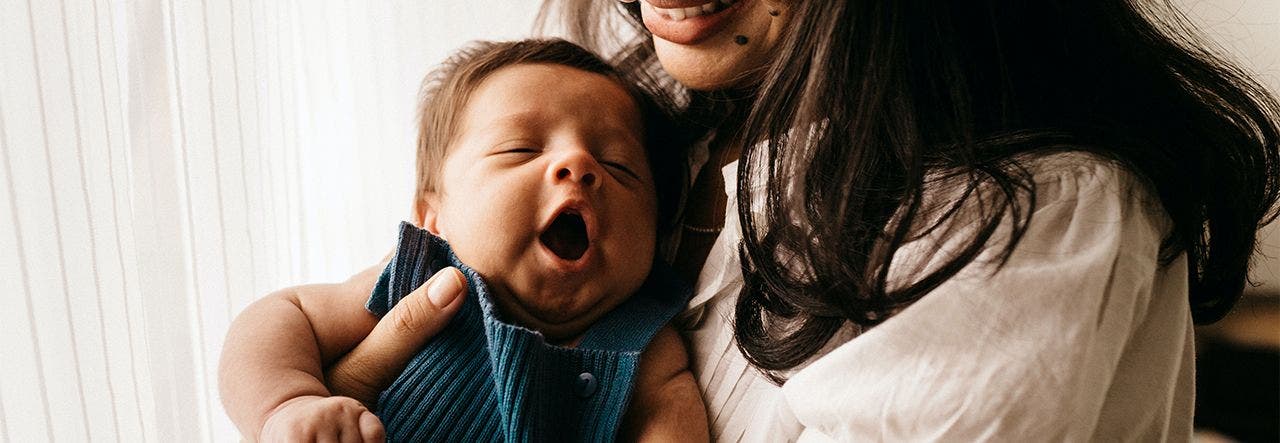 Smiling mother cuddling a yawning infant