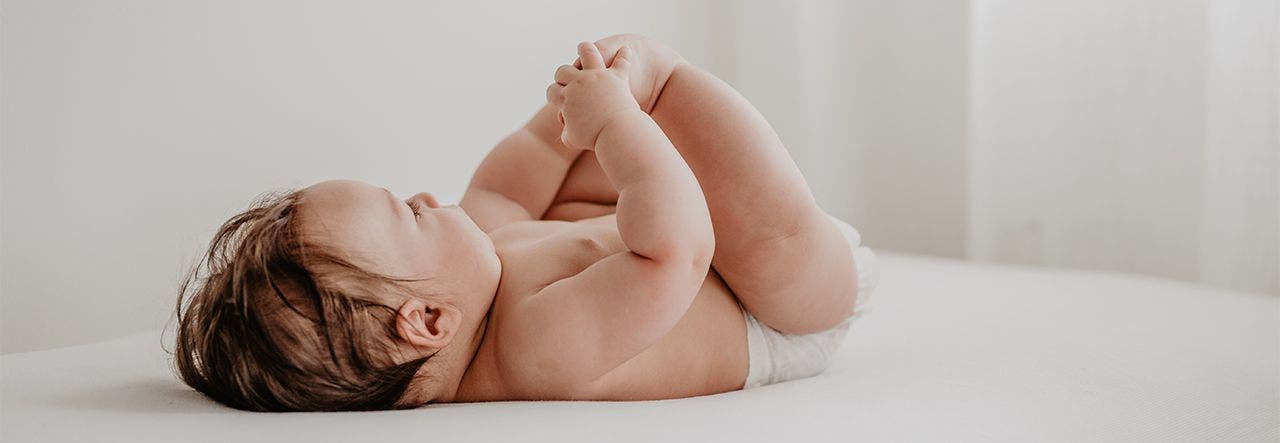 Healthy baby, dressed in just a diaper, playing with their toes