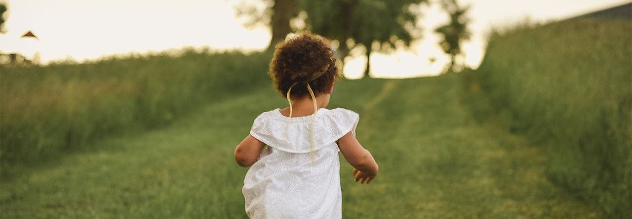 Toddler walking through a grassy field in spring