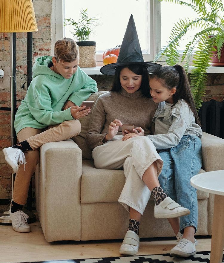 Mom in a witch hat looking at phone with two children