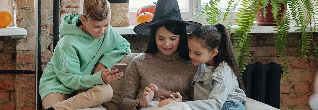 Mom in a witch hat looking at phone with two children