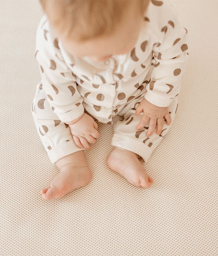 Baby in polka dot onesie sitting on naturepedic breathable crib mattress