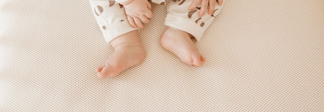 Image of Naturepedic breathable crib mattress with baby feet and hands at the top of the image
