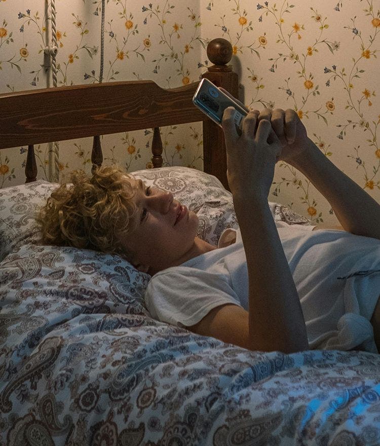 teen looking at cell phone in bed