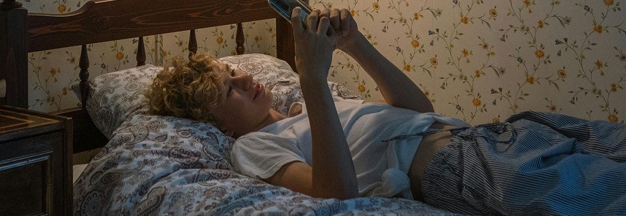 teen looking at cell phone in bed
