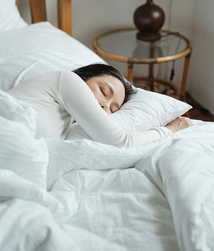 woman sleeping in a bed with white pajamas and white bedding