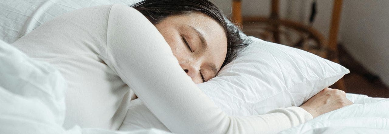 woman sleeping in a bed with white pajamas and white bedding