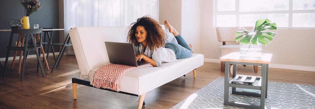 woman laying on futon couch on laptop