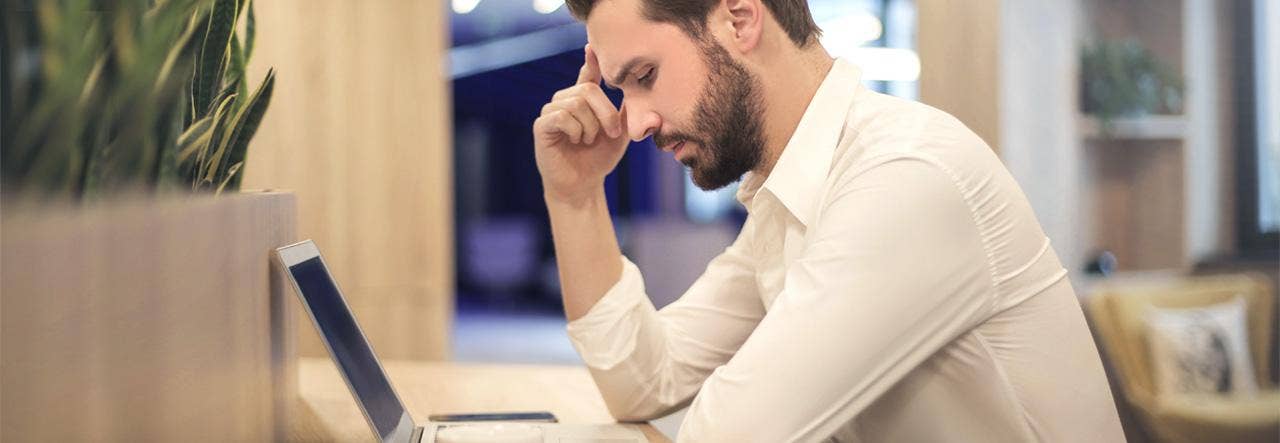 sleep deprived man sitting at laptop with coffee