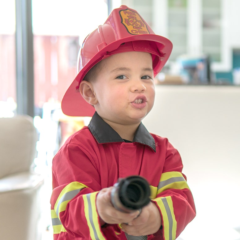 Boy dressed in fireman's costume holding up water hose pretending to spray