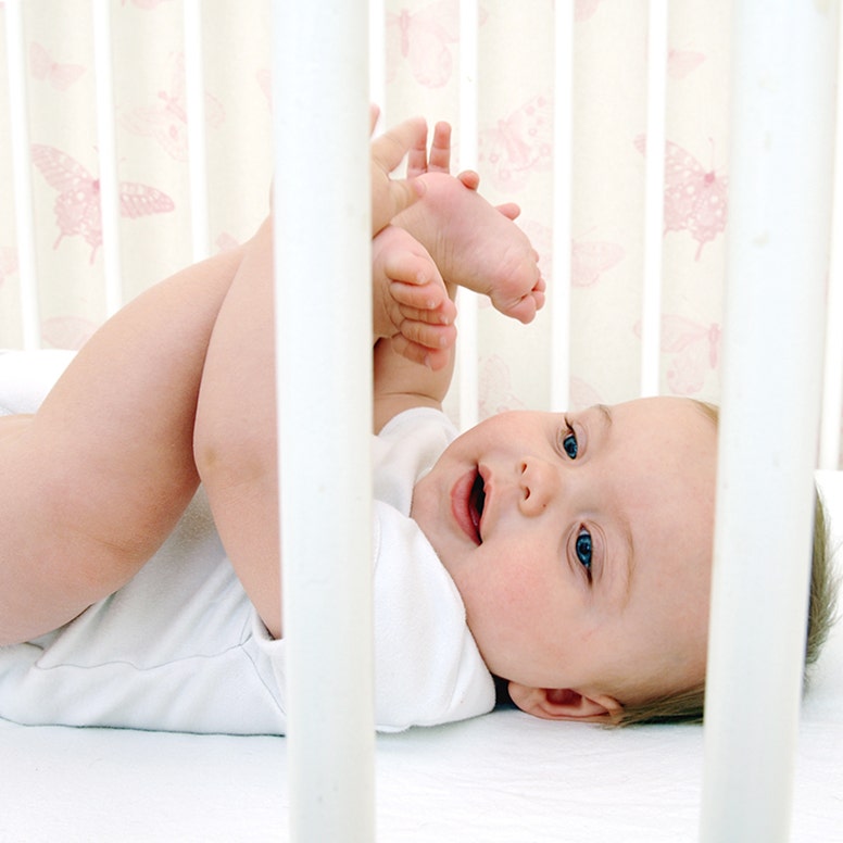 Happy smiling baby laying on back holding up feet in crib