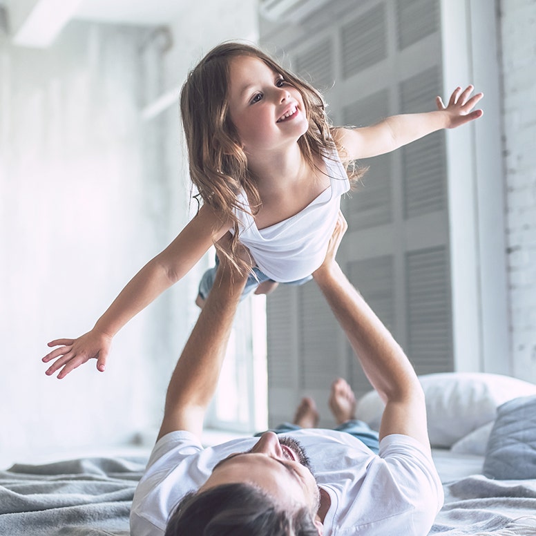 Father laying in bed holding up daughter in flying position