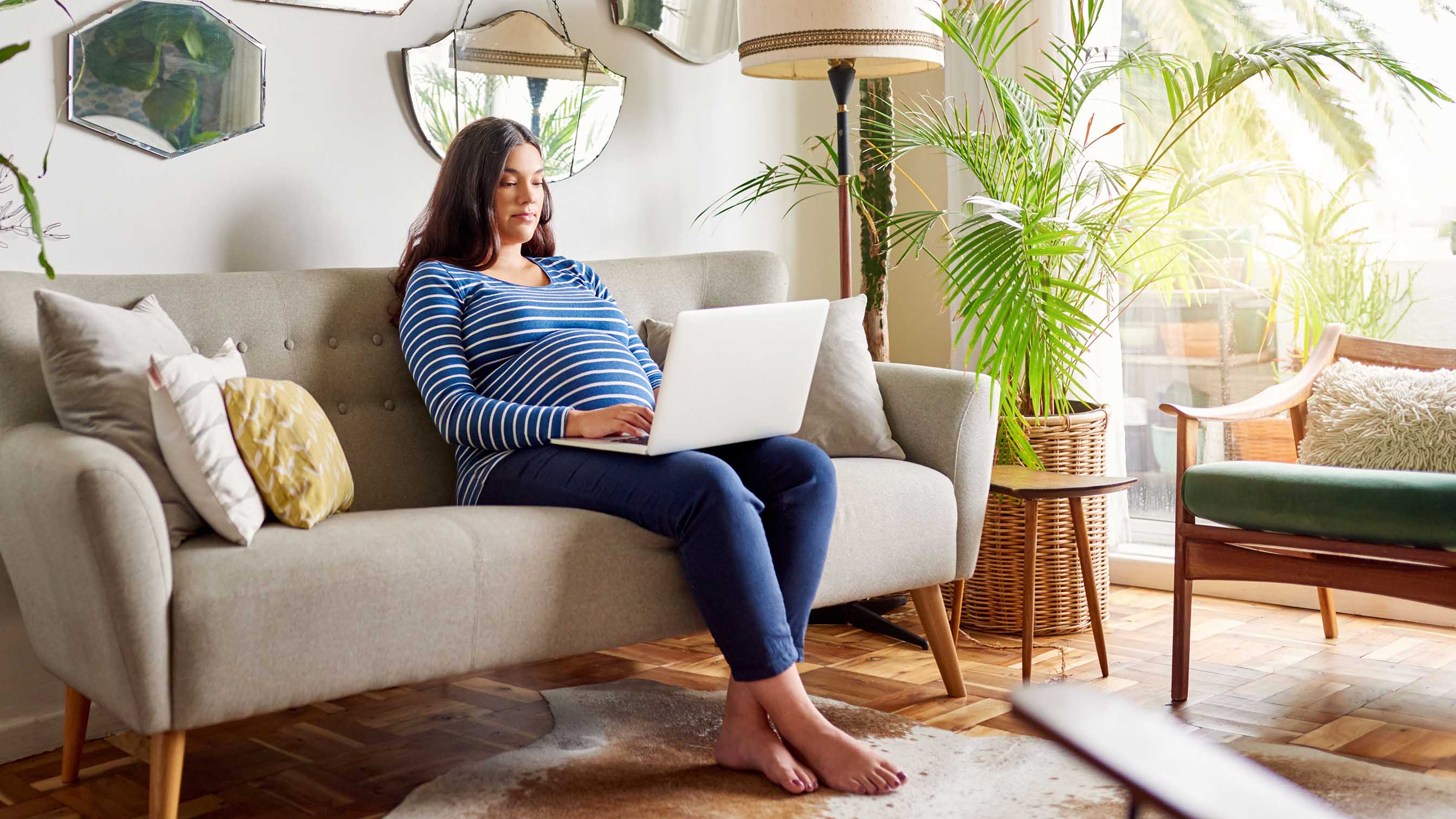 Pregnant woman sitting on a couch and researching on a laptop