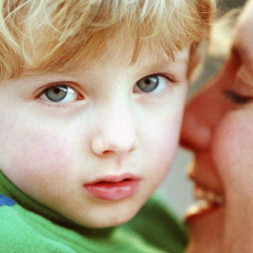 Close-up of boy looking at camera with mother caressing him in background