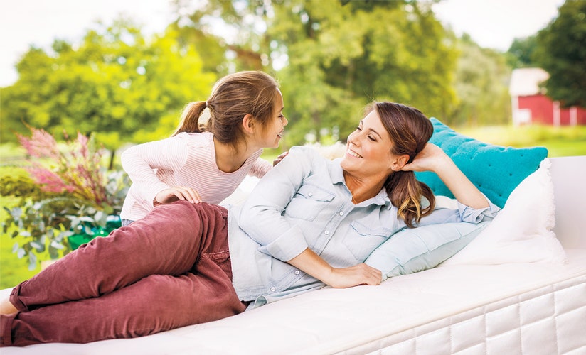 Angled shot of mom and daughter smiling at each other on mattress in outdoor setting