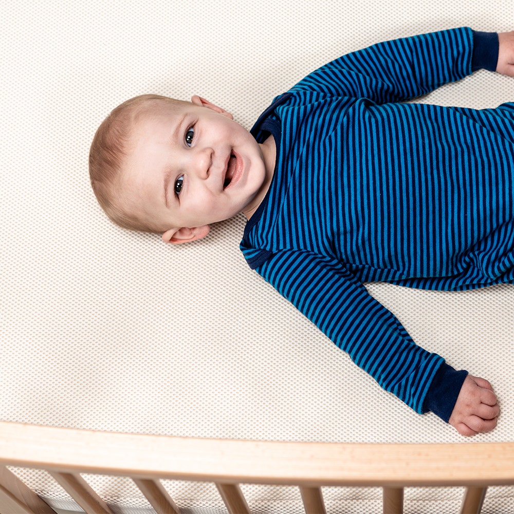 Baby lying on back on oval breathable crib mattress