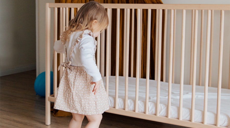 Toddler girl standing next to crib 