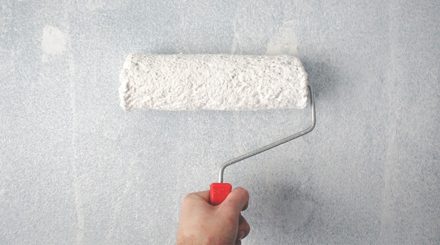 Close-up of person's hand painting a wall with a paint roller