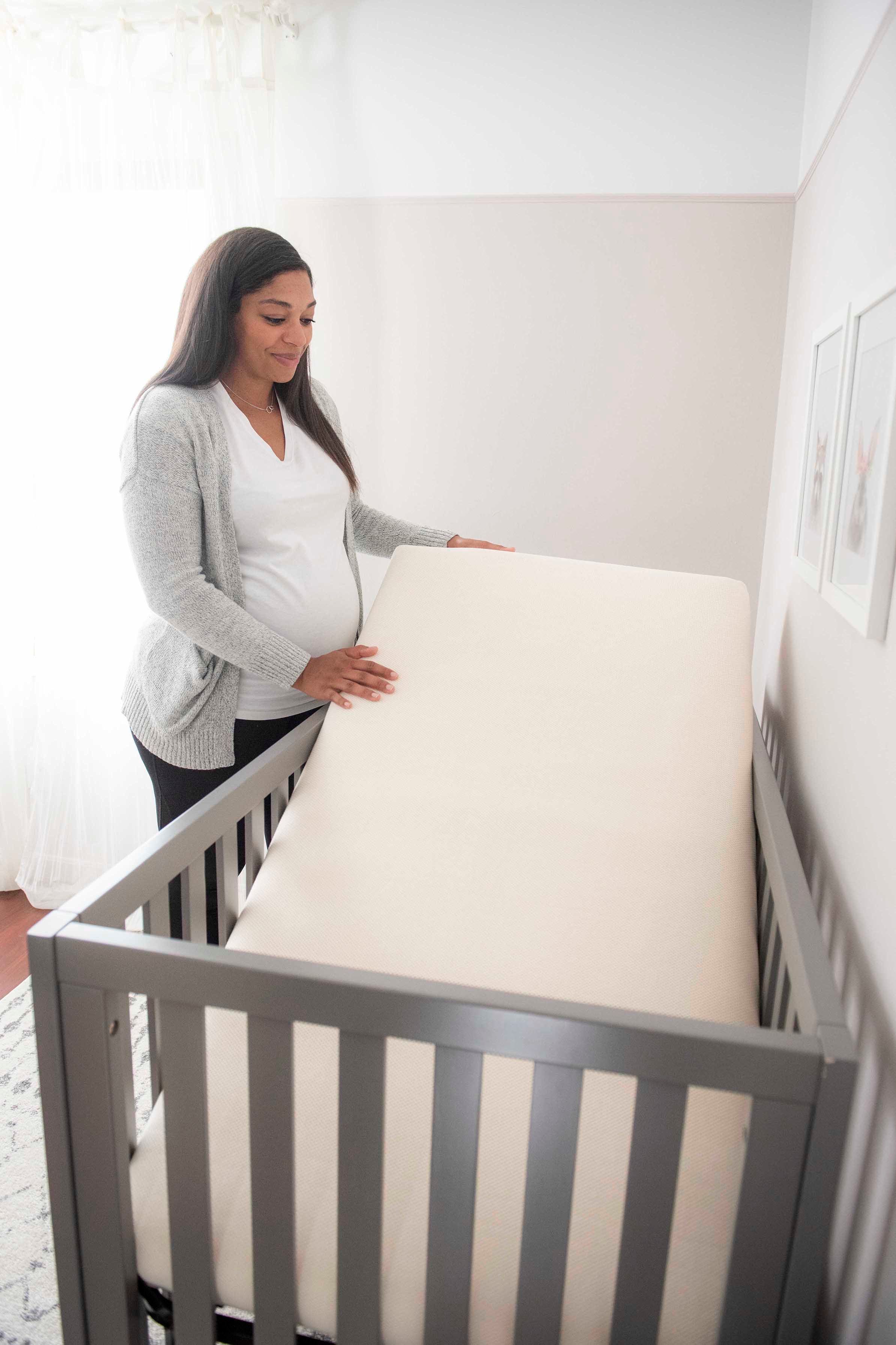 Pregnant woman lifting a Naturepedic crib mattress from the crib