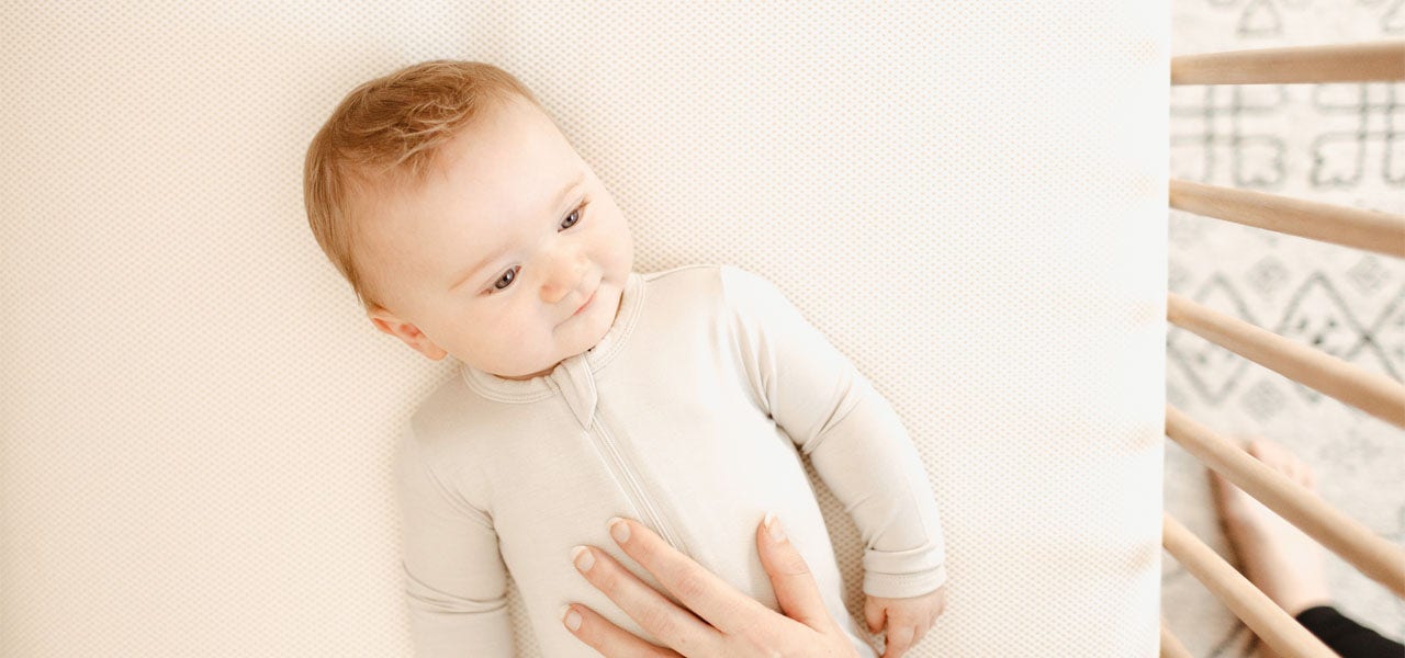 Overhead image of a calm baby on a Naturepedic mattress, woman's hand reaching in