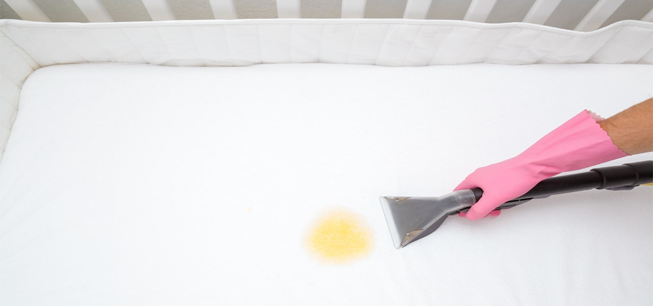 Rubber-gloved hand cleaning a yellow mess off of a crib mattress