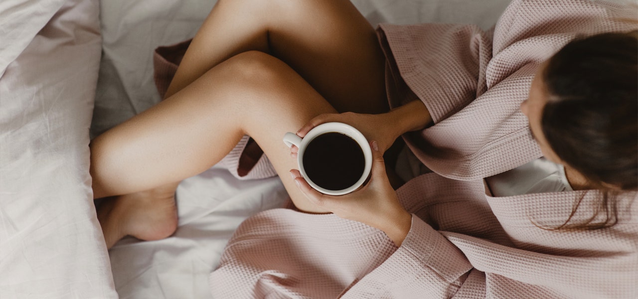 Overhead view of a woman drinking coffee in bed