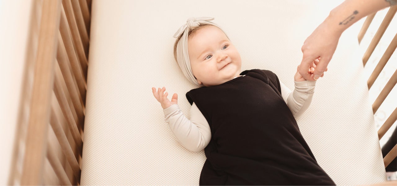 Overhead view of a baby in a crib, smiling up at her mom 