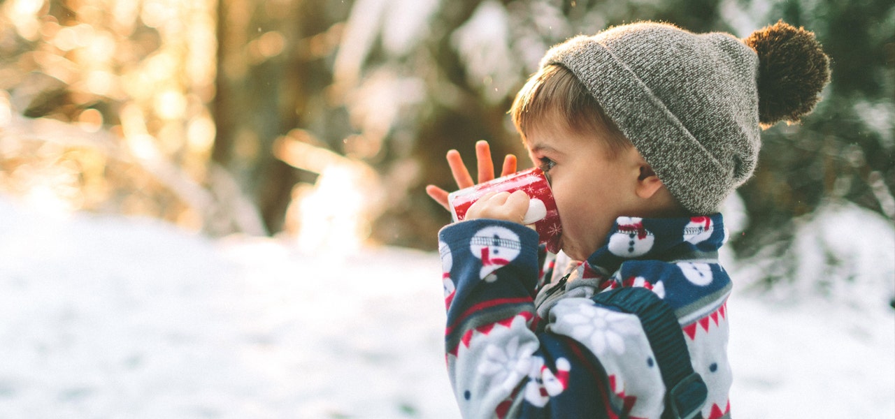 Child wearing pajamas and a hat, drinking hot cocoa outside 